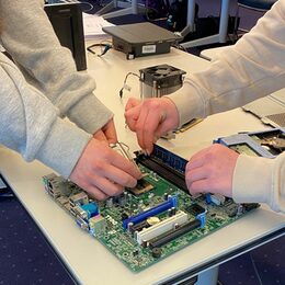 Zwei Paar Mädchenhände arbeiten an einem Computer-Mainboard. Sie halten einzelne Teile in der Hand und stecken es auf der Platine fest.