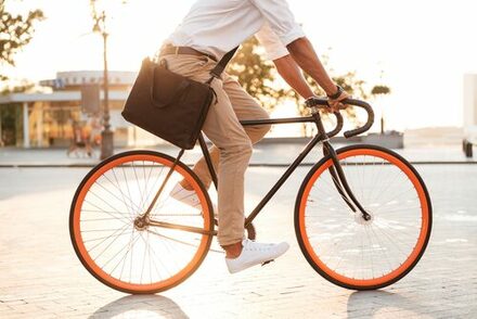 semi-formal gekleideter Mann auf schickem Rennrad mit orangen Felgen im Morgenlicht.