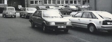 Fahrzeuge in den 1980er Jahren parken auf einem Hof. Ein R4, ein Opel Ascona und andere