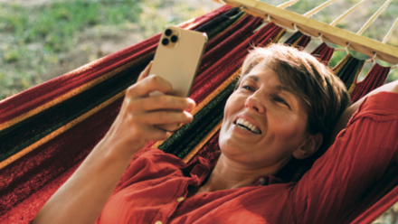 Eine Frau liegt in der Hängematte und schaut auf ihr Handy